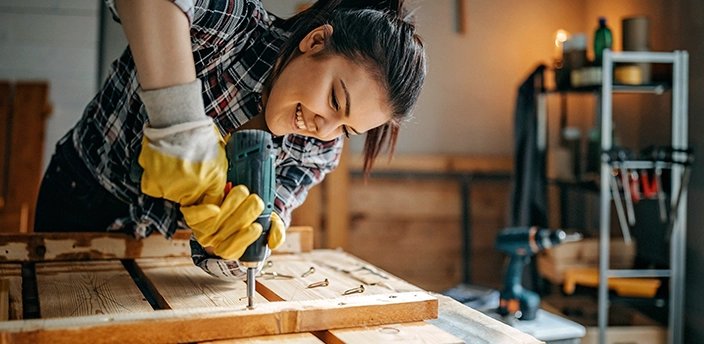 Frau befestigt mit einer Bohrmaschine Holzbalken auf Holzbretter