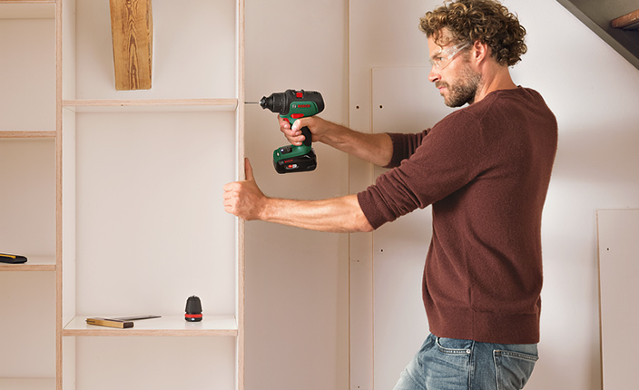 Ein Mann bohrt mit einem Akku Bohrer in ein Regal