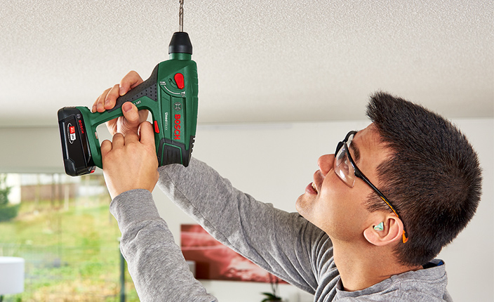 Ein Mann bohrt mit einem Bohrhammer in die Decke von Bosch