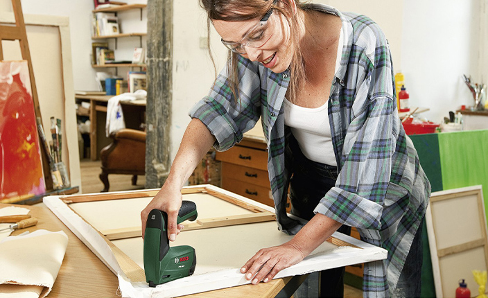 Frau tackert eine Leinwand mit einem Bosch Werkzeug
