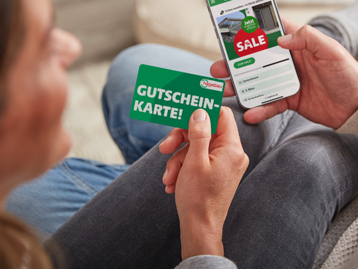 Eine Frau, die die hagebau Gutscheinkarte haptisch in der Hand hält. Ein Mann hält daneben ein Smartphone in der Hand.