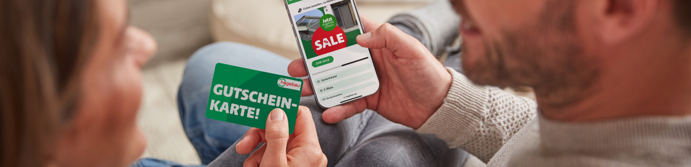 Eine Frau, die die hagebau Gutscheinkarte haptisch in der Hand hält. Ein Mann hält daneben ein Smartphone in der Hand.