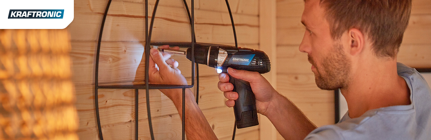 Mann schraubt mit einem Akkuschreiber einen Nagel in eine Holzwand von der Marke Kraftronic