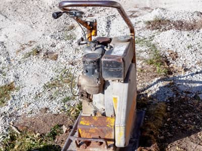 Alte Rüttelplatte auf Kies- und Erduntergrund.