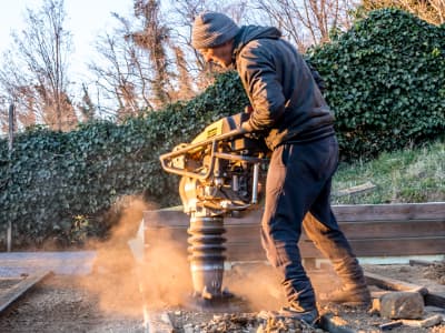 Arbeiter verdichtet Boden mit einem Stampfer auf einer Baustelle.
