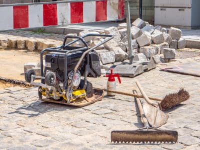 Rüttelplatte mit Werkzeugen auf einer gepflasterten Baustelle.