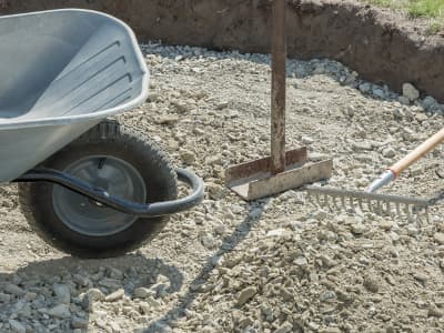 Schubkarre, Rechen und Handstampfer auf Schotterfläche.