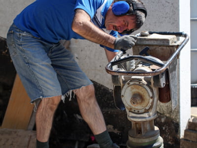 Mann mit Gehörschutz arbeitet an einem Vibrationsstampfer.