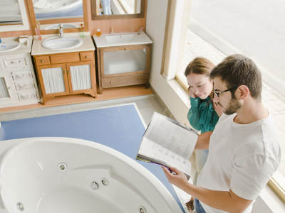 Ein Paar steht in einer Badausstellung und blättert in einem Katalog, während es sich eine moderne Badewanne ansieht