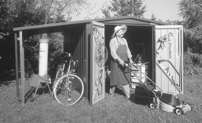 Ein schwarz und weiß Bild von einem älteren Mann der aus einem Gartengeräteschuppen rauskommt