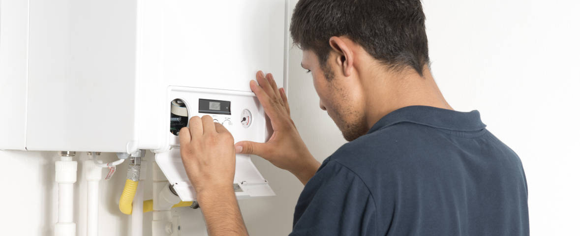 Ein Mann steht vor einem weißen Wandgerät und prüft dessen Einstellungen. Das Gerät dient zur Steuerung von Heizung oder Warmwasser.