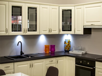 Eckküche mit weißen Schränken, schwarzer Arbeitsplatte und Unterbauleuchten.