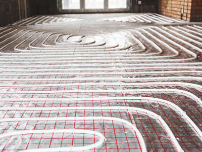 In einem Rohbau sind Heizungsrohre einer Fußbodenheizung auf einem Gitter verlegt. Die Rohre verlaufen in regelmäßigen Schleifen über den gesamten Boden.