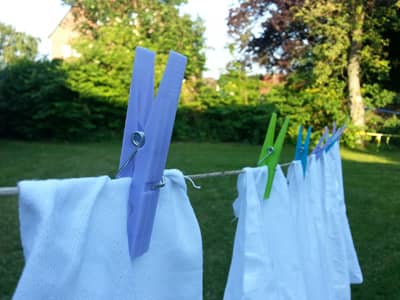 Weiße Wäschestücke, die auf einer Wäscheleine im Garten hängen und mit Wäscheklammern befestigt sind