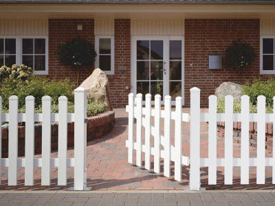 Weißer Gartenzaun mit offenem Tor vor einem Hauseingang.