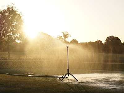 Foto einer großen Beregnungsanlage, die eine Rasenfläche weitläufig mit Wasser besprüht