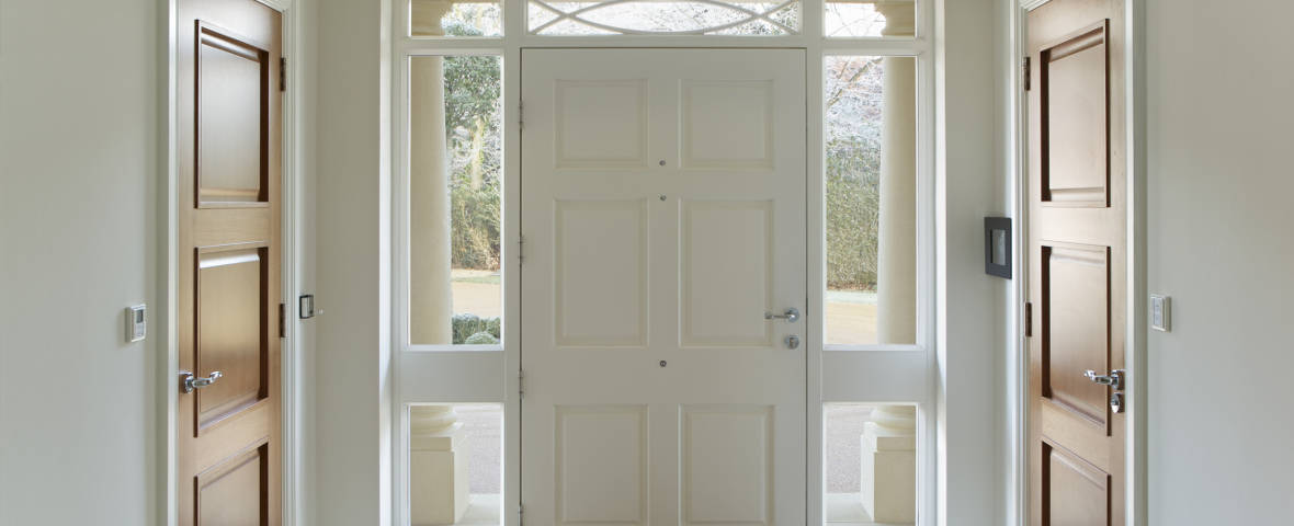 Foto einer weißen Eingangstür von innen, links und rechts sind zwei Zimmertüren aus Holz zu sehen