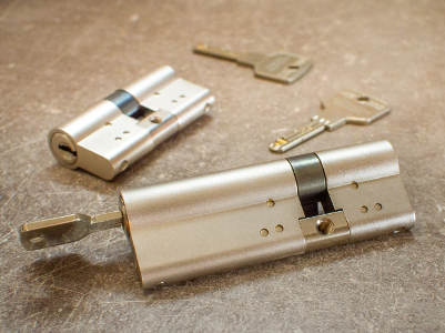 Nahaufnahme von zwei Türzylindern mit dazugehörigen Schlüsseln auf einer Werkbank, in einem der Zylinder steckt der passende Schlüssel