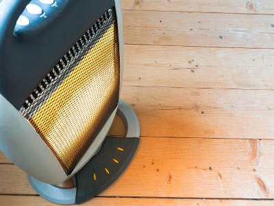 Ein elektrischer Heizstrahler mit leuchtendem Heizelement steht auf einem Holzboden