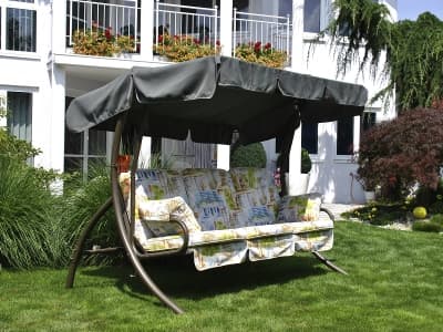 Eine Hollywoodschaukel mit Polstern und einem Sonnendach in einem Garten