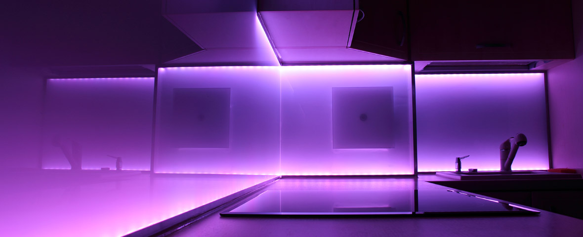 Eine moderne Küche wird durch violette LED-Lichtleisten unter den Hängeschränken violett beleuchtet
