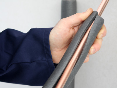 Eine Hand bringt eine Dämmhülle aus Schaumstoff an einem Kupferrohr an