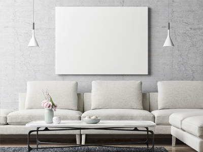 Ein modern eingerichtetes Wohnzimmer zeigt ein helles Sofa vor einer grauen Wand. Darüber hängt ein leeres weißes Bild, und auf dem Couchtisch stehen eine Vase mit Blumen und eine Schale.