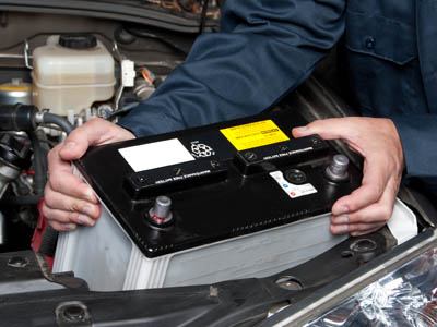 Detailaufnahme einer geöffneten Motorhaube und Händen, die die Autobatterie entnehmen