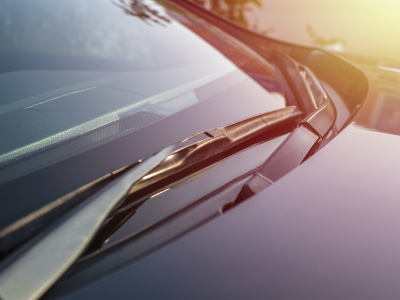 Ein Scheibenwischer liegt auf der sauberen Frontscheibe eines Autos in der Sonne. Die Szene ist in warmes Licht getaucht, was auf einen Sonnenaufgang oder -untergang hinweist