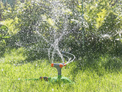 Foto eines Gartensprengers, der in einem weiten Bogen feine Wasserstrahlen auf einer Rasenfläche verteilt