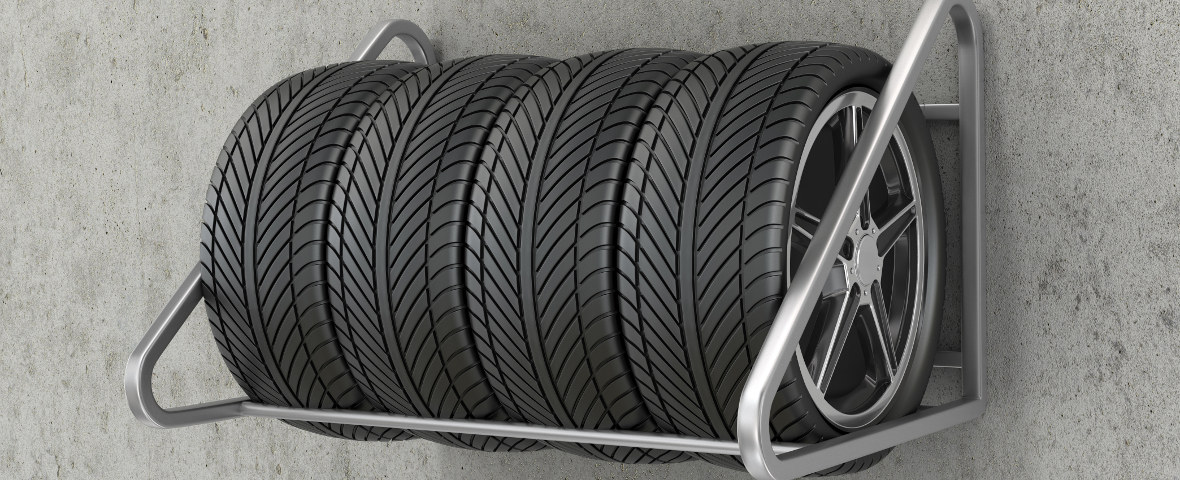 Vier Autoreifen mit Felgen sind auf einem silbernen Felgenbaum aus Metall gelagert. Der Reifenständer steht vor einer grauen Betonwand