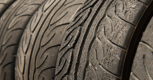 Mehrere stark abgenutzte Autoreifen mit deutlich sichtbarem Profilverschleiß stehen nebeneinander. Die Nahaufnahme zeigt Risse und Glättung in der Lauffläche