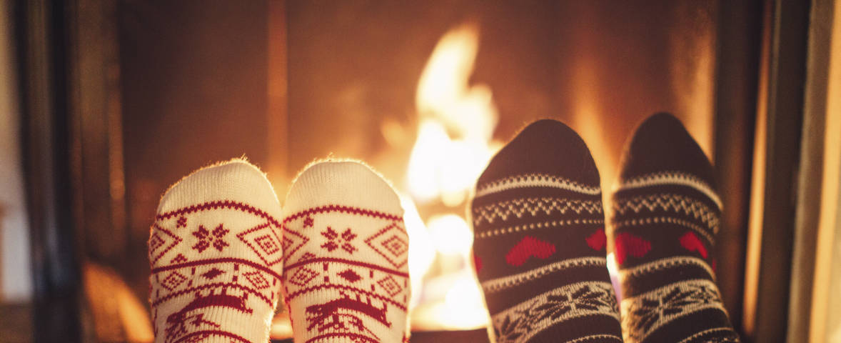 Zwei Paar Füße in winterlichen Socken liegen entspannt vor einem brennenden Kaminfeuer