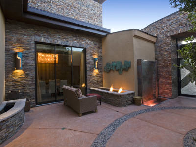 Eine stilvoll gestaltete Terrasse mit Natursteinwänden, integriertem Kaminfeuer und indirekter Wandbeleuchtung. Die Terrasse ist mit einem Sofa ausgestattet und grenzt an große Glasschiebetüren